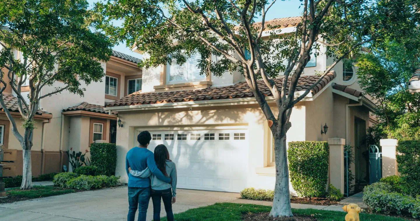 Couple standing arm in arm looking at a two storey house with a garage
