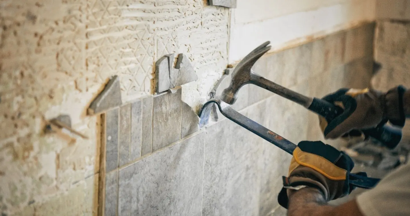 Tradesperson using a hammer and chisel to remove old wall tiles during a renovation